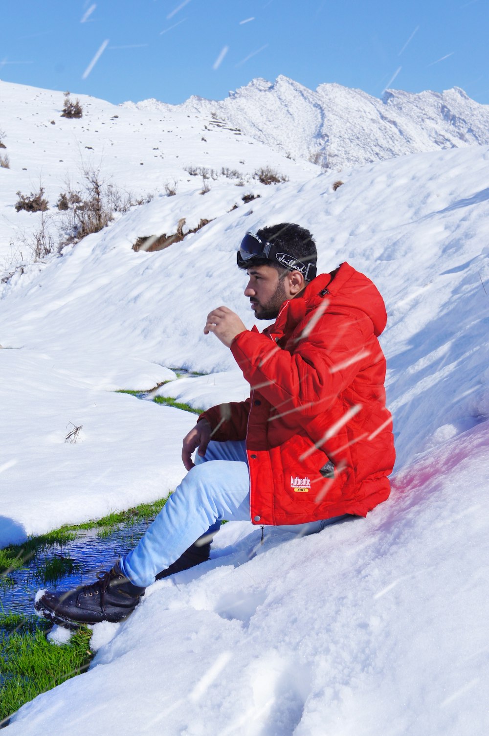 man in red jacket and blue pants sitting on snow covered ground during daytime