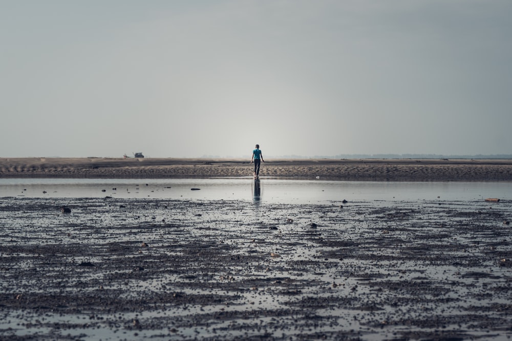 Persona con chaqueta negra caminando sobre arena marrón durante el día