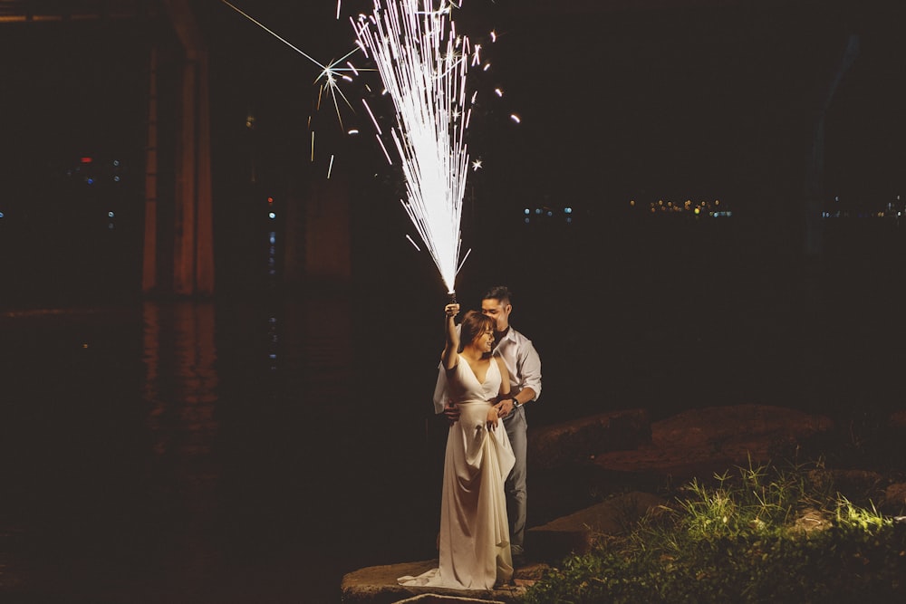 woman in white dress holding white dandelion flower near body of water during night time