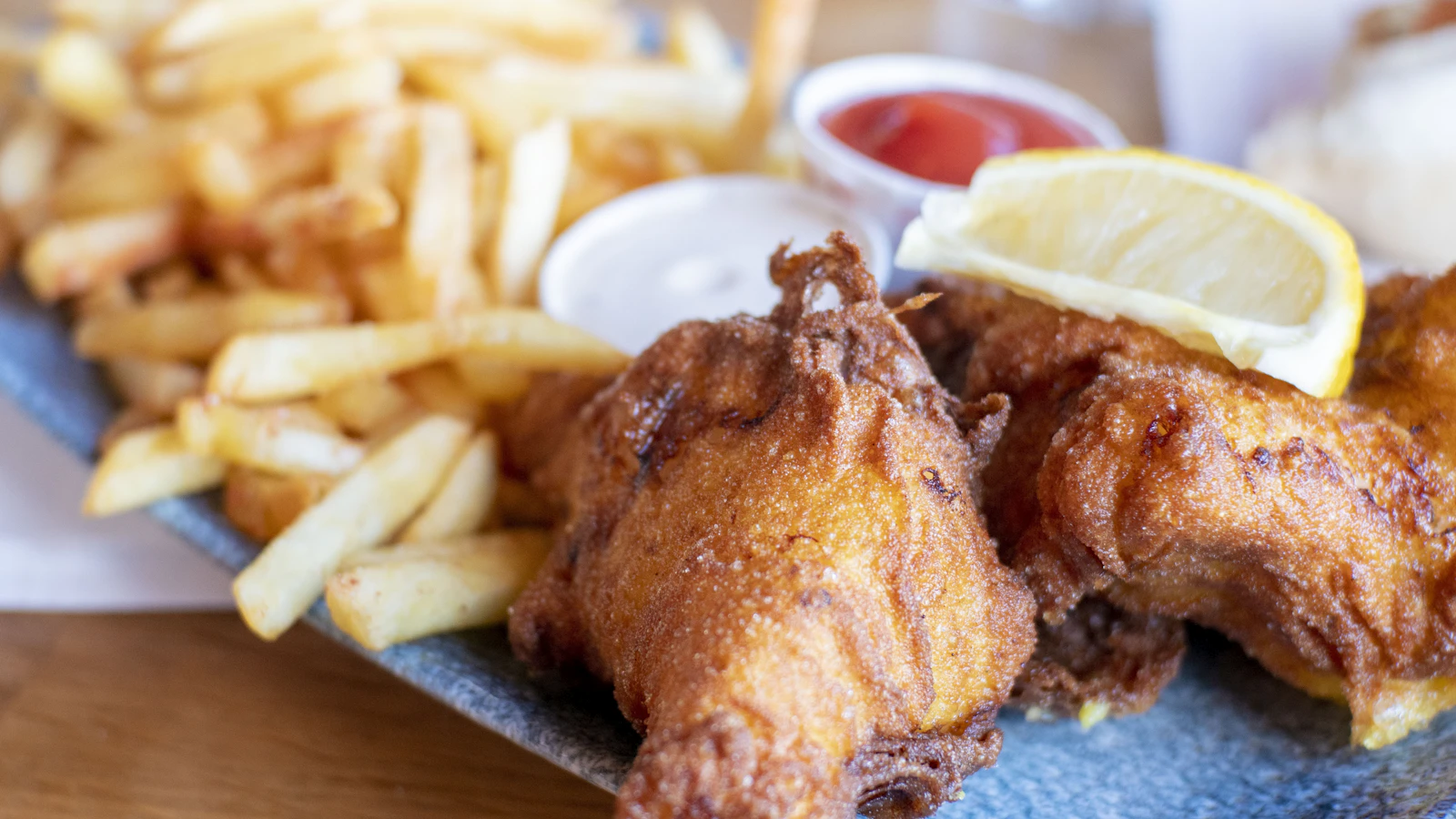 Close-up of crispy battered fish and chips with a lemon wedge, ketchup and tartar sauce on a blue plate
