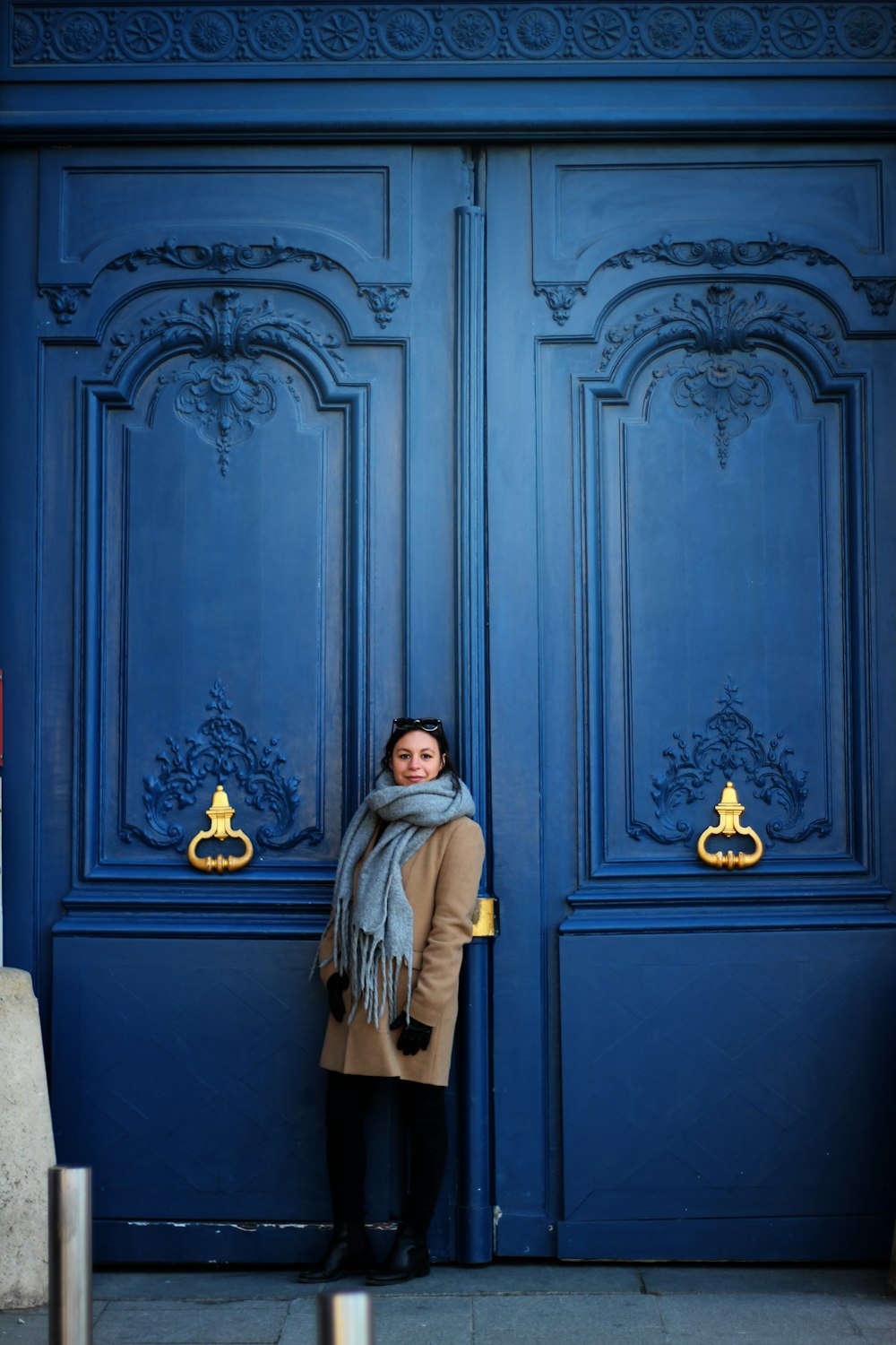 woman in brown coat standing beside blue wooden door