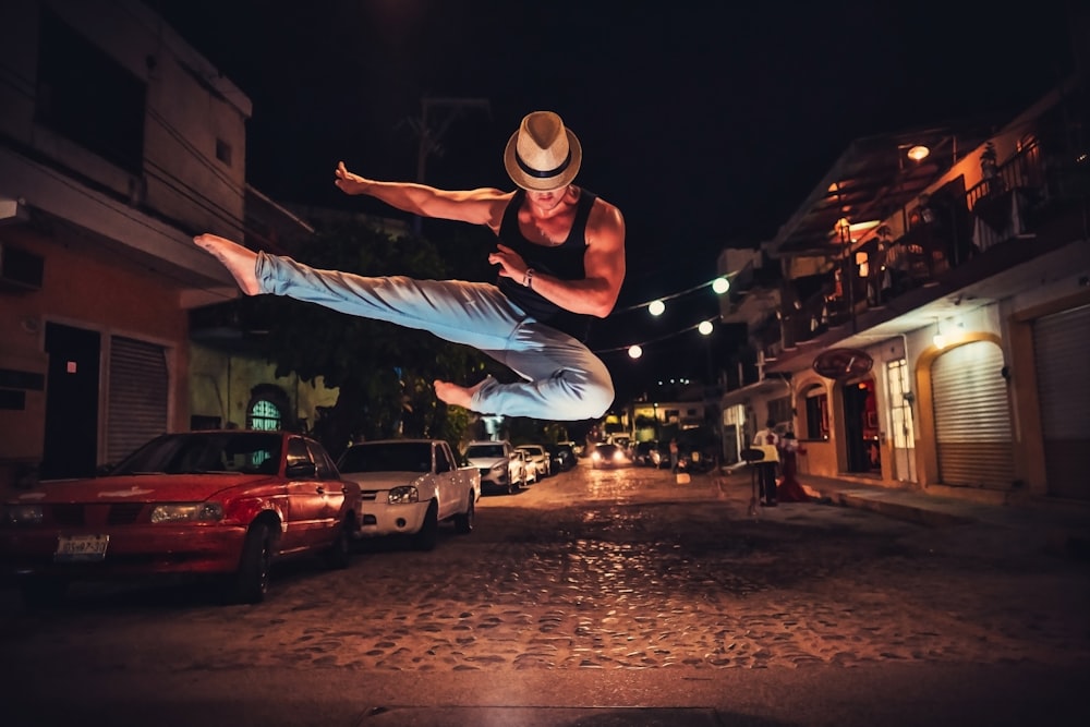 白いカウボーイハットをかぶった男が夜の街路で飛び跳ねる