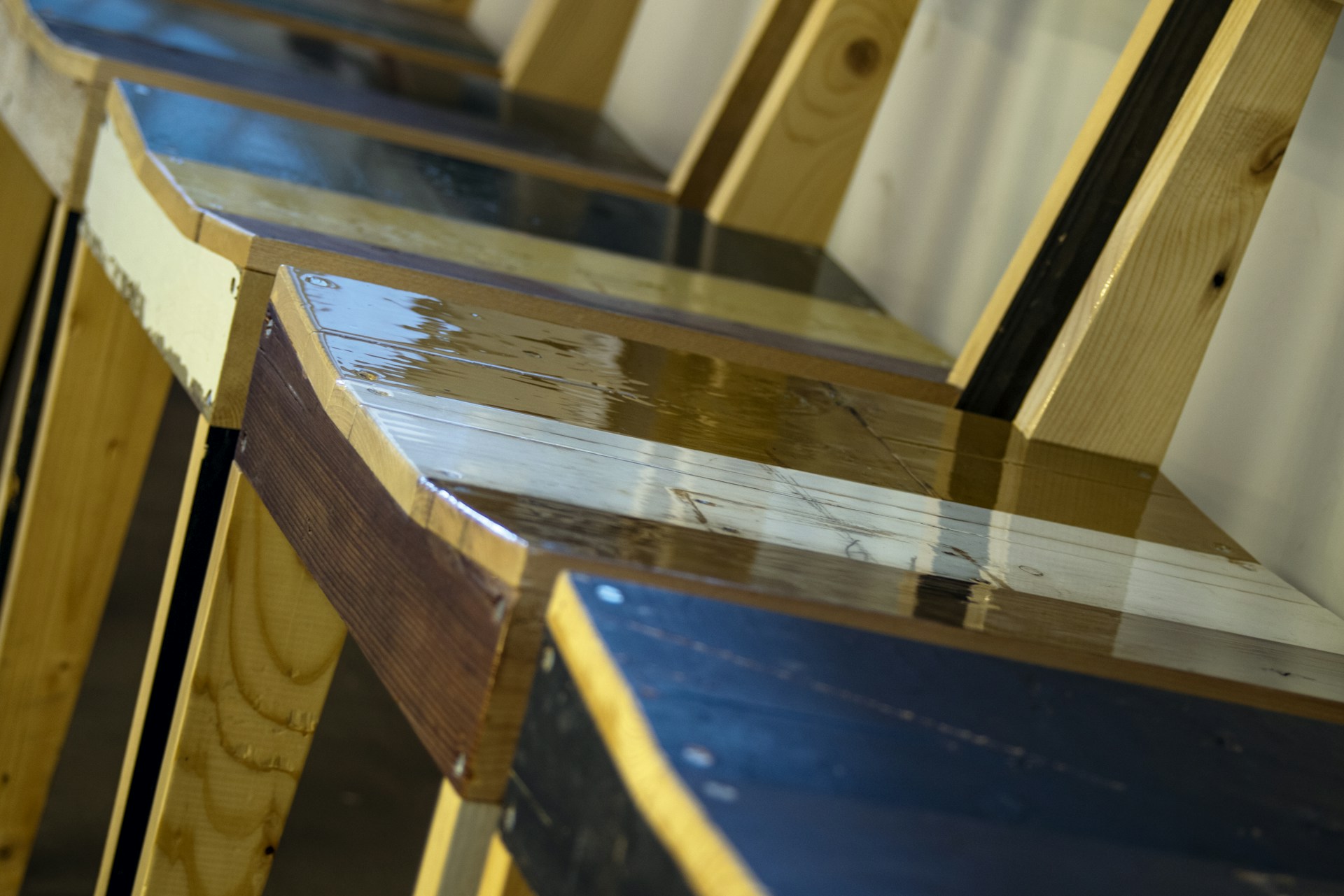 A row of freshly refinished wooden furniture pieces drying under soft workshop lighting.