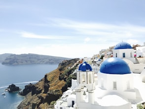 white and blue concrete building on brown rock formation near body of water during daytime