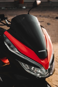 A close-up view of a motorcycle's front, featuring a sleek design with a glossy black and red color scheme. The Honda logo is prominently displayed above the headlights.