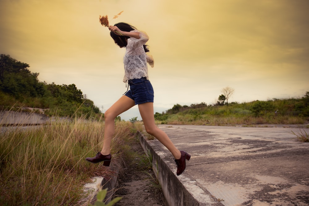 woman in white shirt and blue denim shorts standing on brown wooden dock during daytime