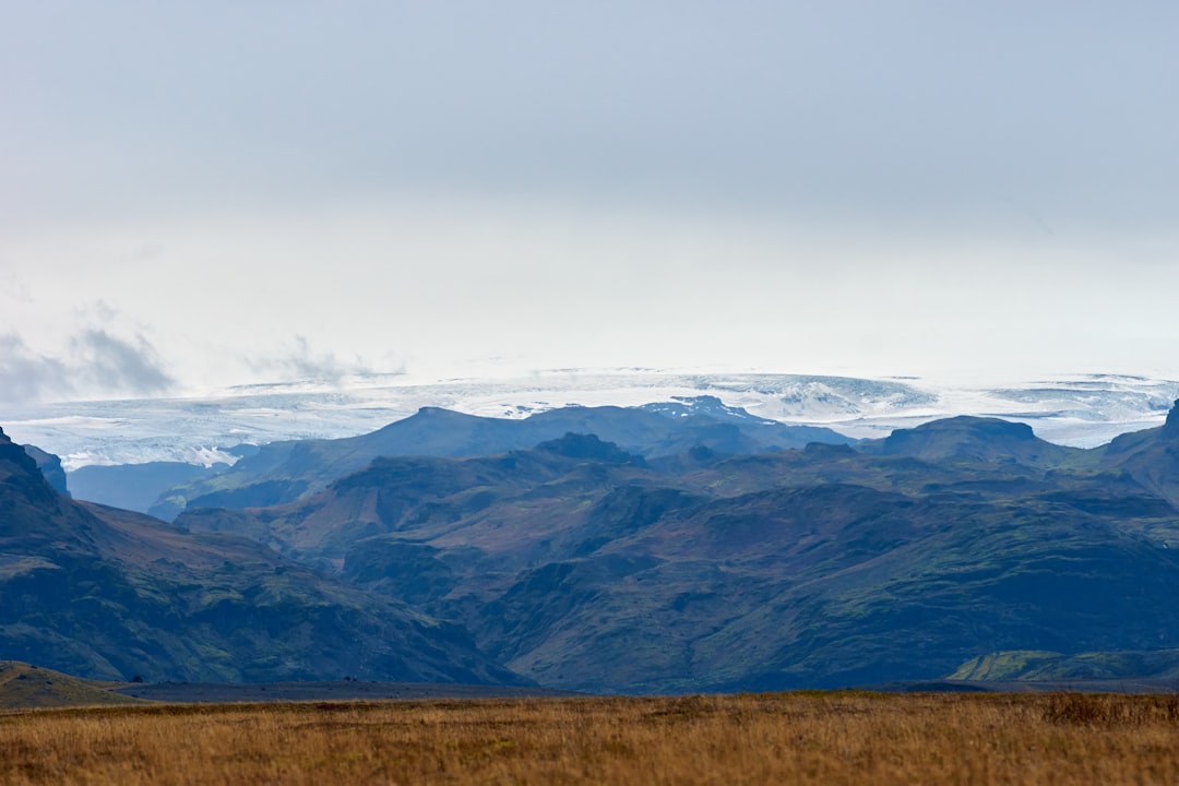 brown grass field near mountains under white clouds during daytime