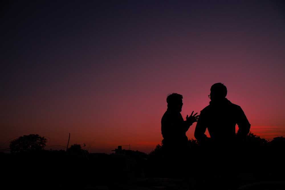 silhouette of 2 men sitting on ground during sunset