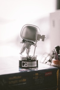A silver astronaut figurine holding a flag stands on a black base labeled MTV Video Music Award. The scene is lit softly, with a blurred background that includes part of a workspace or shelf.