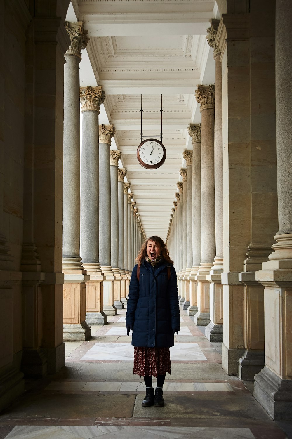 woman in blue coat standing near white concrete pillar during daytime