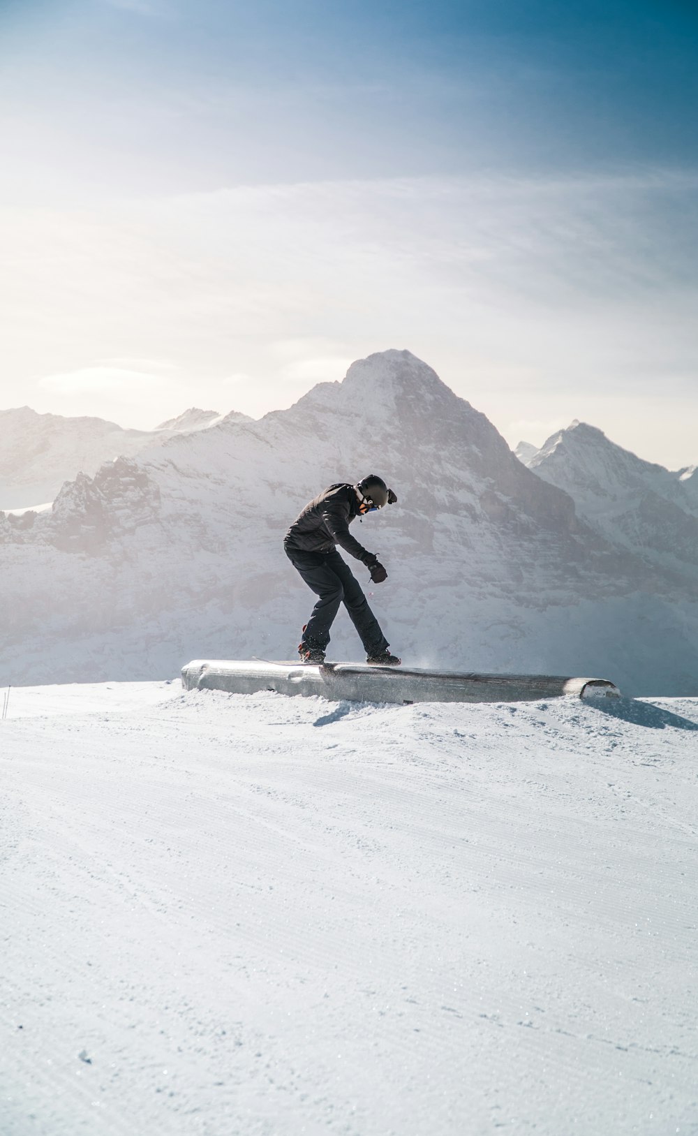 man in black jacket and black pants riding on snowboard on snow covered mountain during daytime