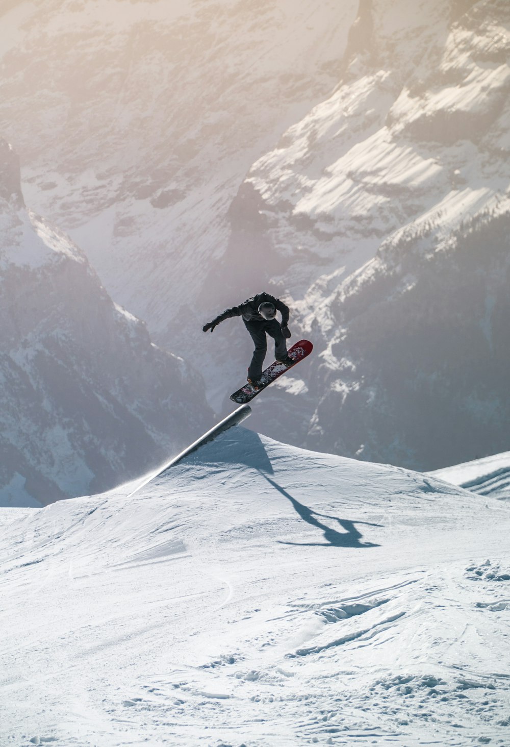 빨간 재킷과 검은 바지를 입은 남자가 눈 덮인 산에서 스키 블레이드를 타고