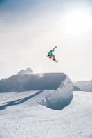 A snowscoot rider launching off a snowy mountain jump against a clear blue sky in Crans-Montana.