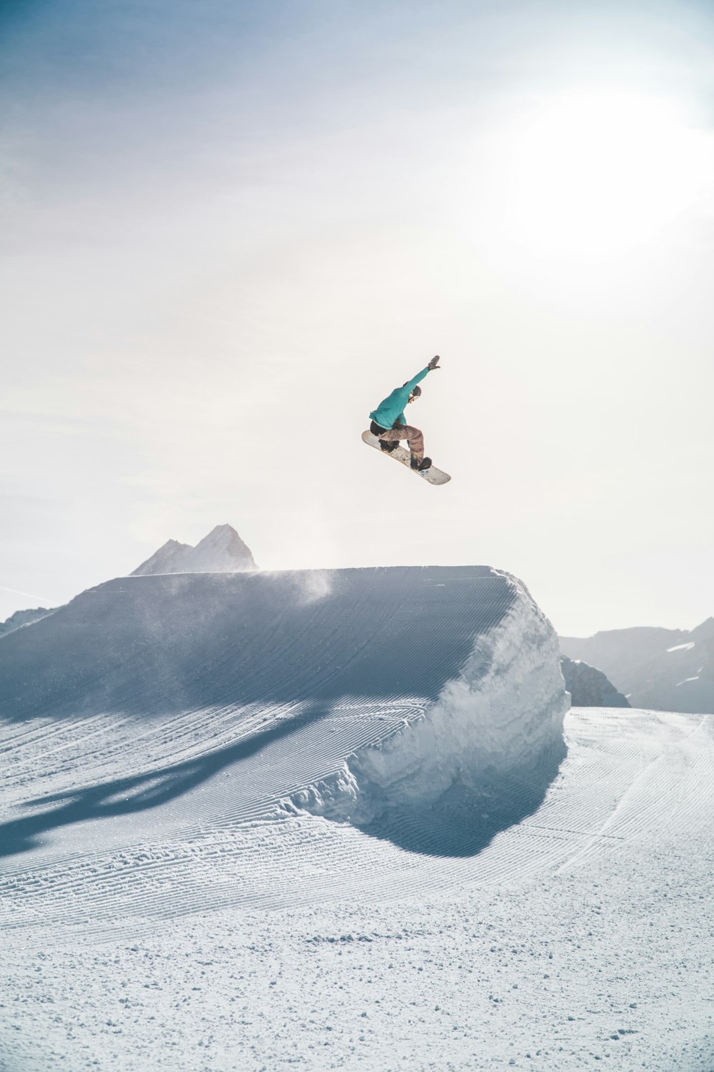 Mann in schwarzer Jacke und blauer Jeans springt tagsüber auf den schneebedeckten Berg