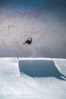 A skier mid-air performing a jump against a backdrop of rugged mountain cliffs.