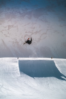 A skier mid-air performing a jump against a backdrop of rugged mountain cliffs.