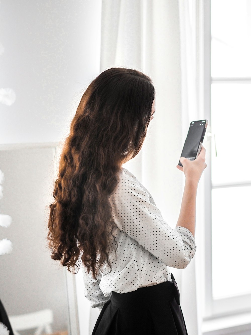 Femme en chemise à manches longues blanche et noire tenant un smartphone argenté