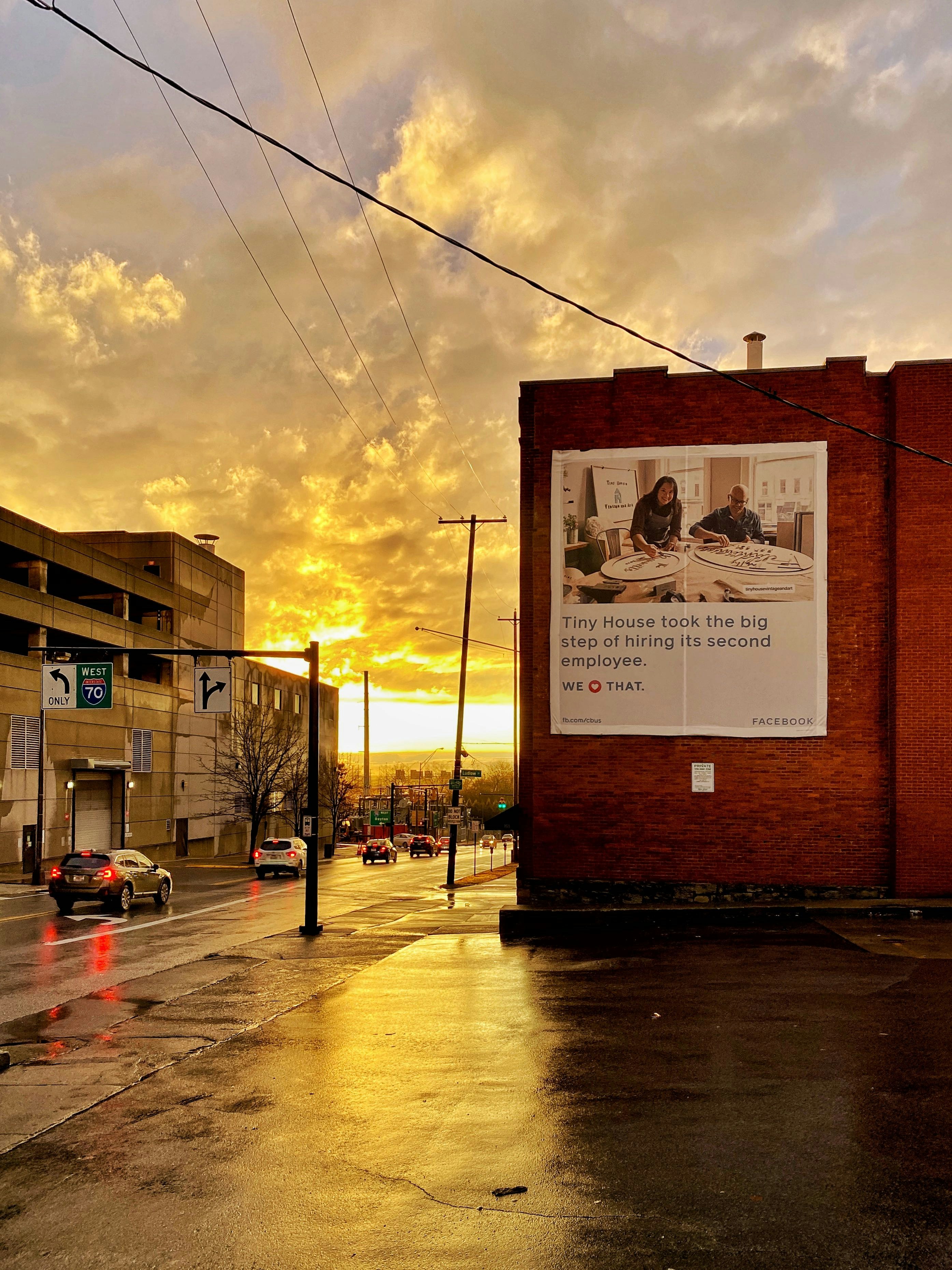 Large outdoor billboard on busy highway at golden hour, dramatic sky, bold advertisement graphics visible from distance