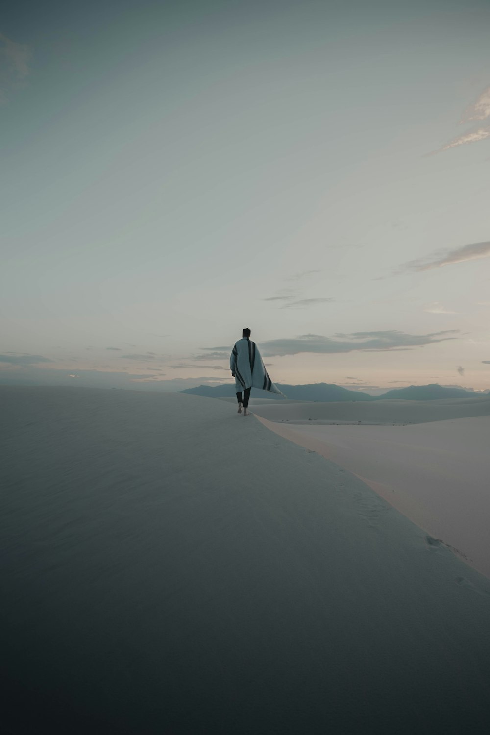 man in white long sleeve shirt walking on gray sand during daytime