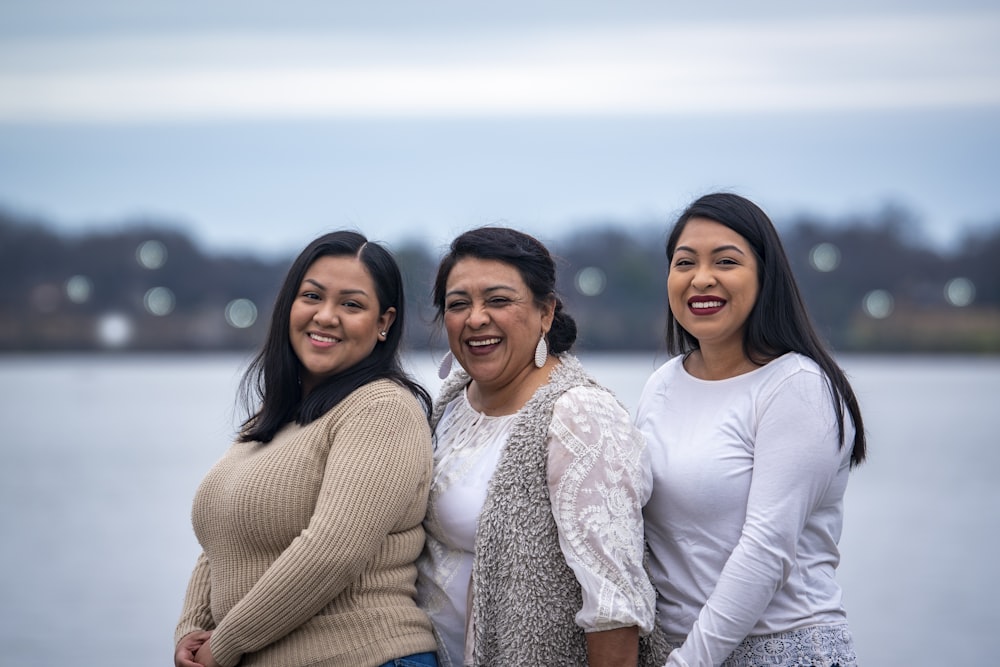 2 women smiling and standing near body of water during daytime