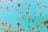 A close-up view of a rusted metal surface with a turquoise-colored paint that is peeling and worn. Brown rust patches are scattered across the surface, creating an aged and textured appearance.