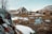A rustic cabin is nestled in a mountainous landscape, surrounded by snow-covered ground and rocky terrain. In the foreground, a small stream winds through the area, providing a sense of tranquility. Bare trees are scattered around, adding to the serene, wintery setting.