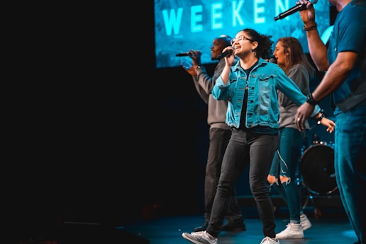 A group of friends joyfully singing karaoke with microphones and a screen displaying lyrics