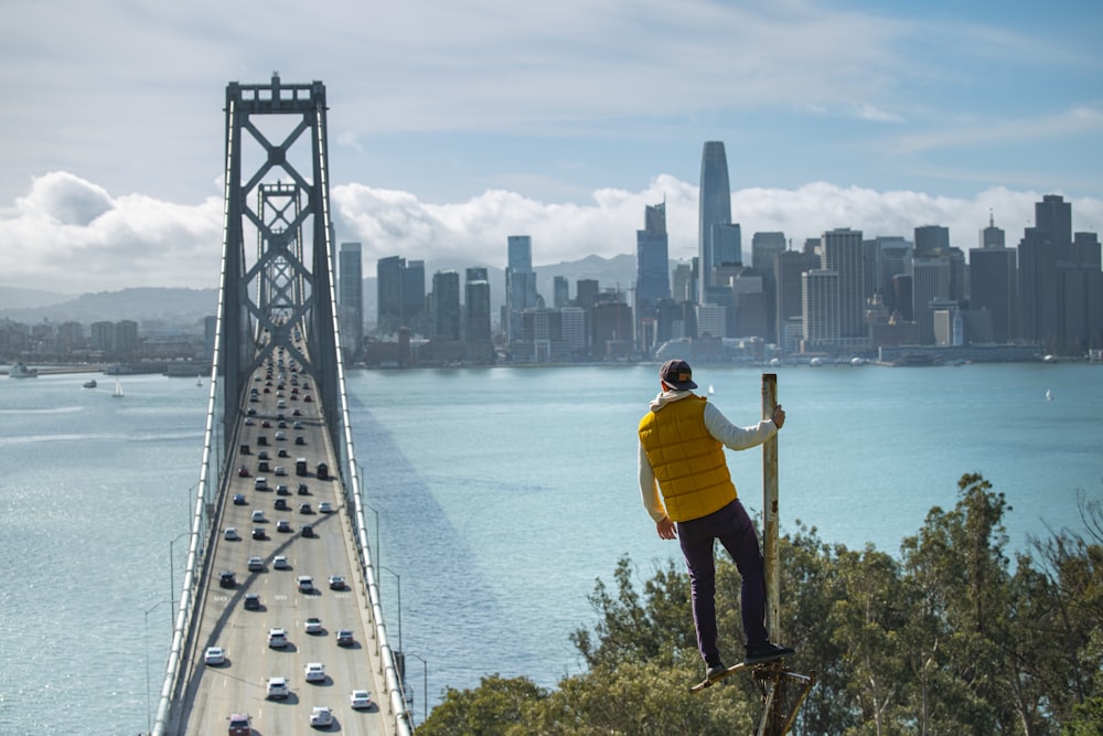 man in yellow hoodie and black pants standing on wooden dock during daytime