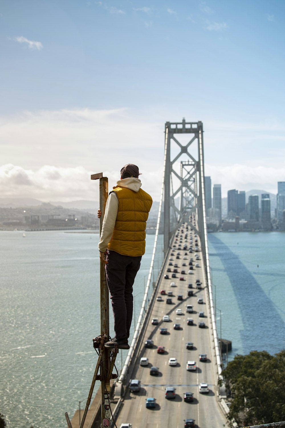 uomo in giacca gialla e pantaloni marroni in piedi sul ponte durante il giorno