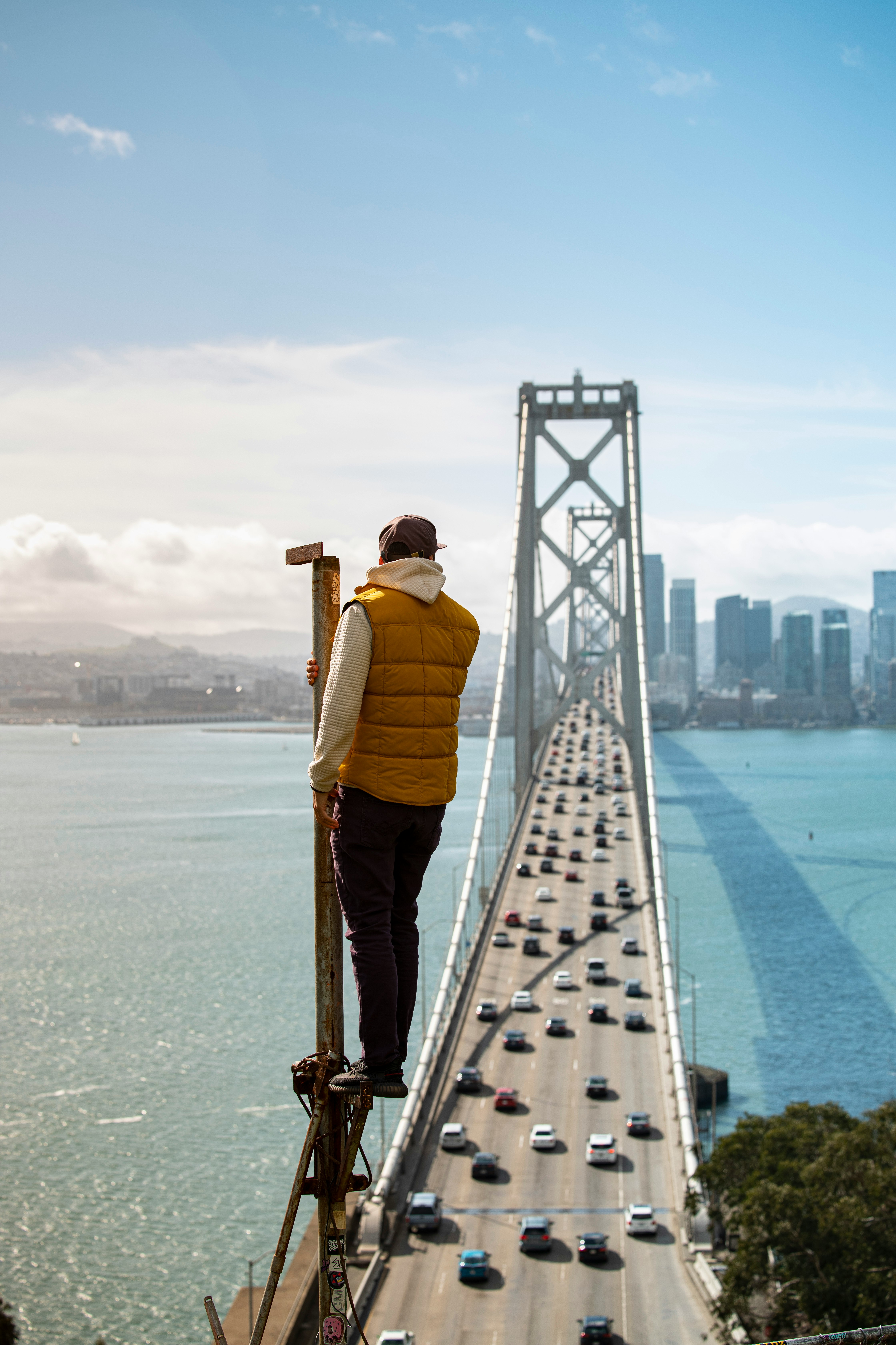 man in yellow jacket and brown pants standing on bridge during daytime