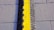 A bright yellow and black cable protector placed on a gray pavement with visible concrete slabs and seams.