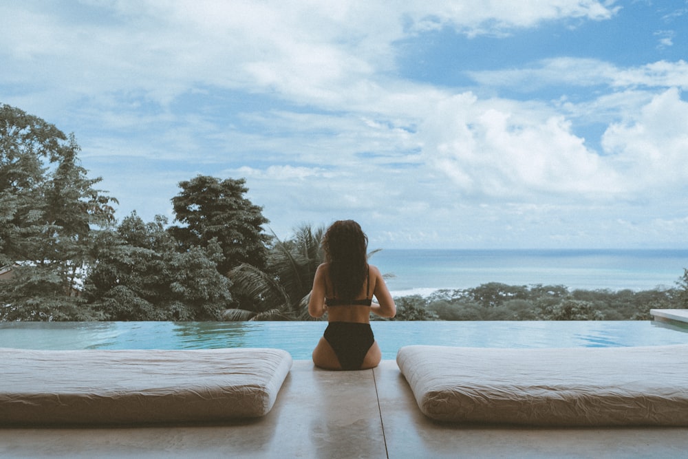 woman in black bikini sitting on brown wooden dock during daytime