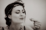 A woman with dark hair tied back and wearing a decorative headband and earrings is looking at a small item held in her hand, possibly food or a trinket. Her makeup is done in a vintage style, and the image has a sepia tone, giving it a nostalgic feel.