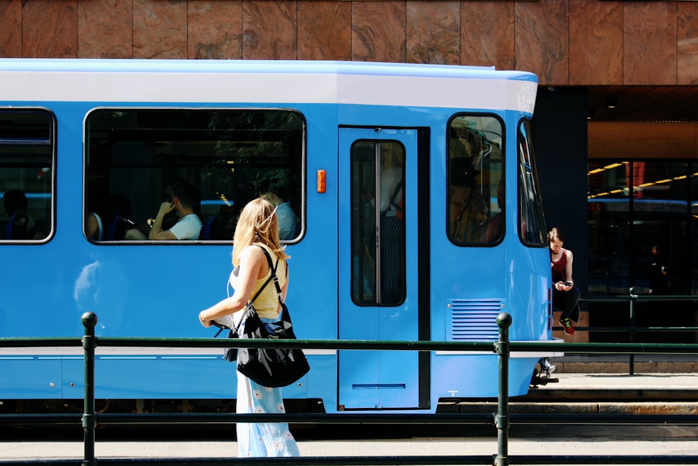 woman in black leather backpack standing beside blue and white train during daytime