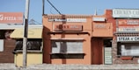 A row of small, rustic restaurants and shops with colorful signs, including a pizza place, lemonade stand, and chicken cafe. The buildings have a vintage aesthetic with signs advertising various foods like steak, cheese, and drinks.