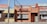 A row of small, rustic restaurants and shops with colorful signs, including a pizza place, lemonade stand, and chicken cafe. The buildings have a vintage aesthetic with signs advertising various foods like steak, cheese, and drinks.