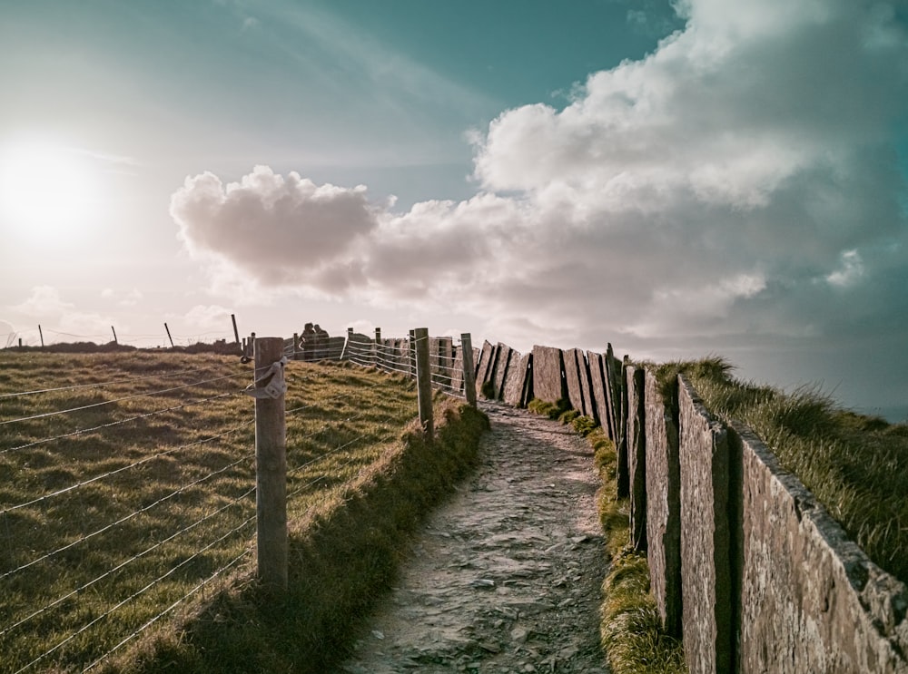 brown wooden fence on green grass field under white clouds and blue sky during daytime