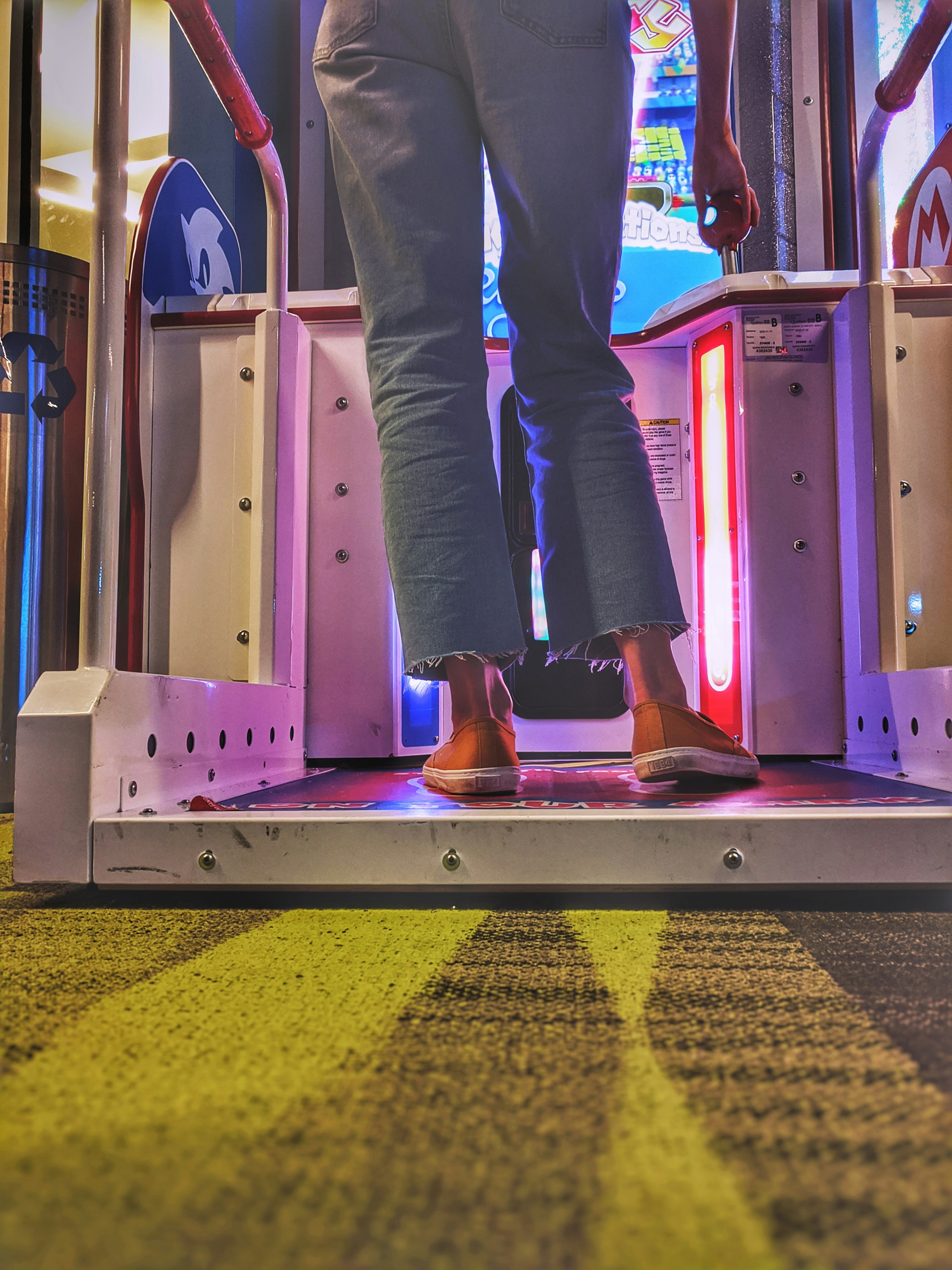 Young woman standing and playing on a videogame arcade machine.