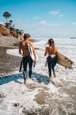 woman in white tank top and black pants holding white surfboard standing on beach during daytime