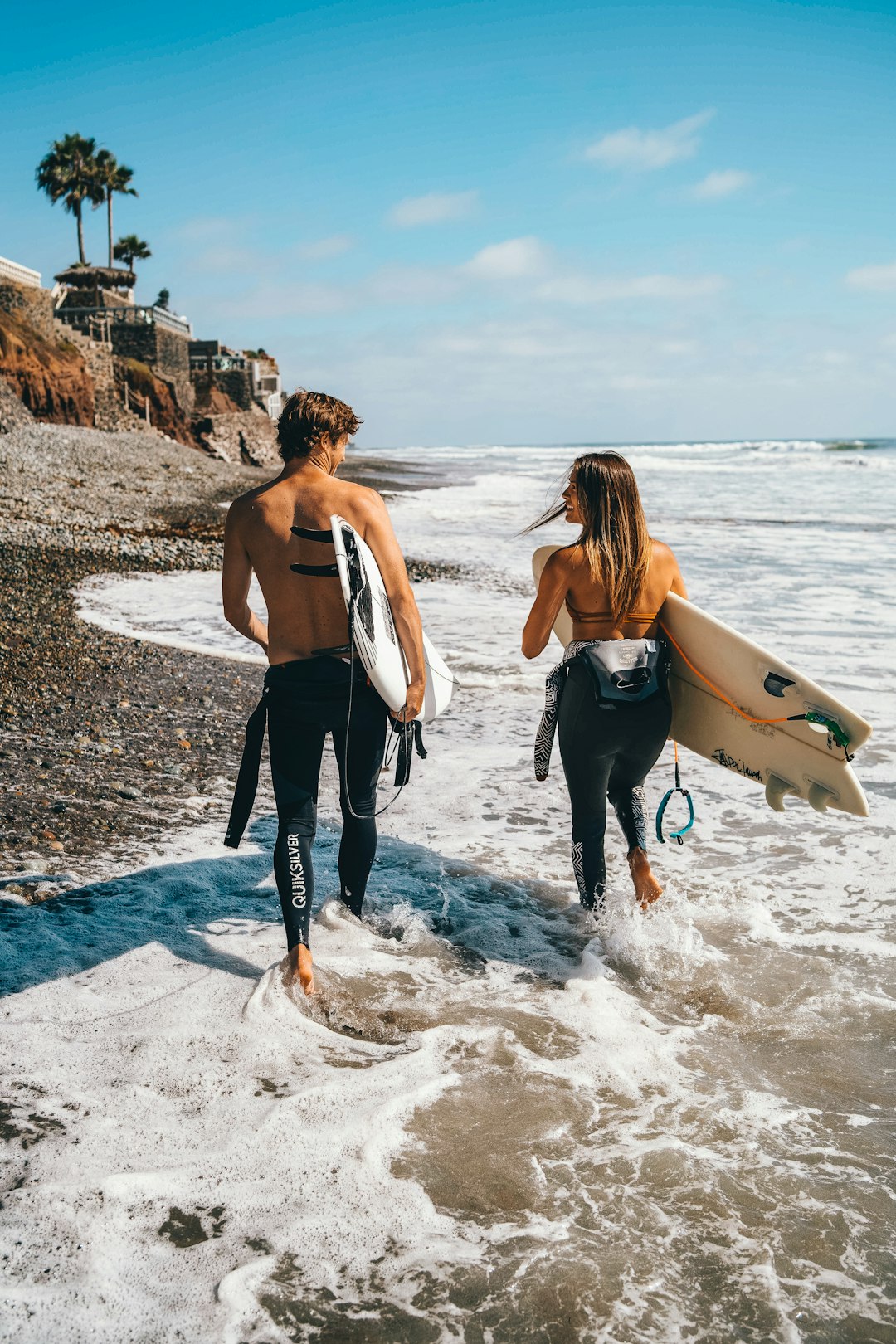 woman in white tank top and black pants holding white surfboard standing on beach during daytime