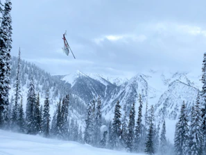 A close-up of a Shaktiyatra helicopter landing on a mountain helipad amid pine trees.