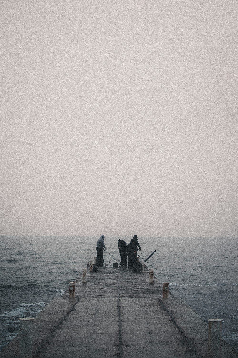 3 men sitting on brown wooden dock during daytime