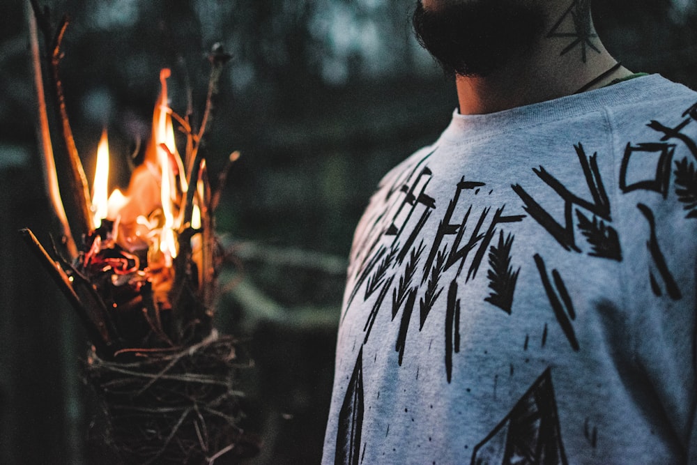 man in gray and black crew neck shirt standing near bonfire during daytime