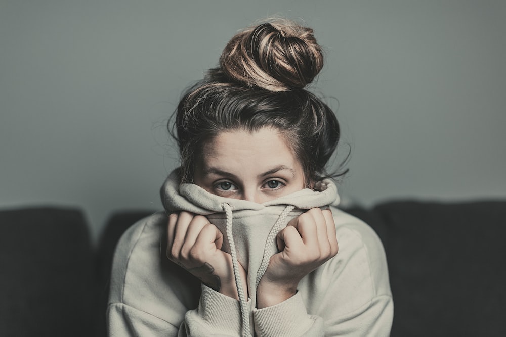 woman in white hoodie covering her face with her hands