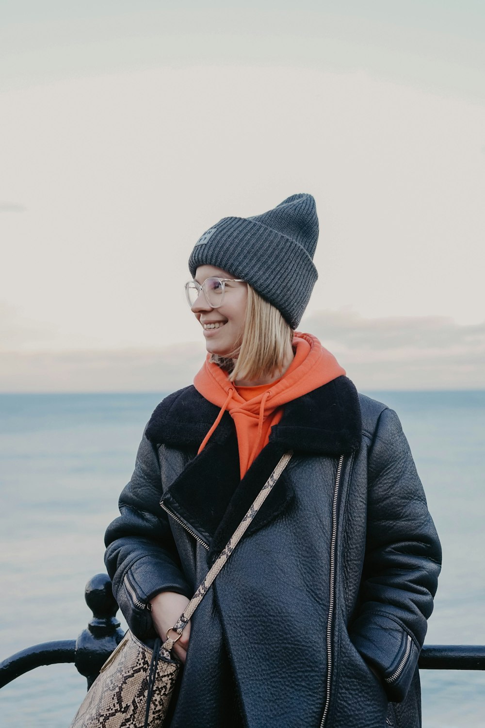 woman in black knit cap and gray coat standing on beach during daytime