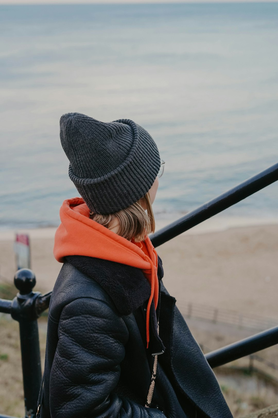 woman in gray knit cap and red hoodie looking at the sea during daytime