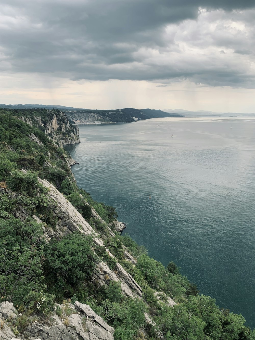 green and brown mountain beside body of water under cloudy sky during daytime