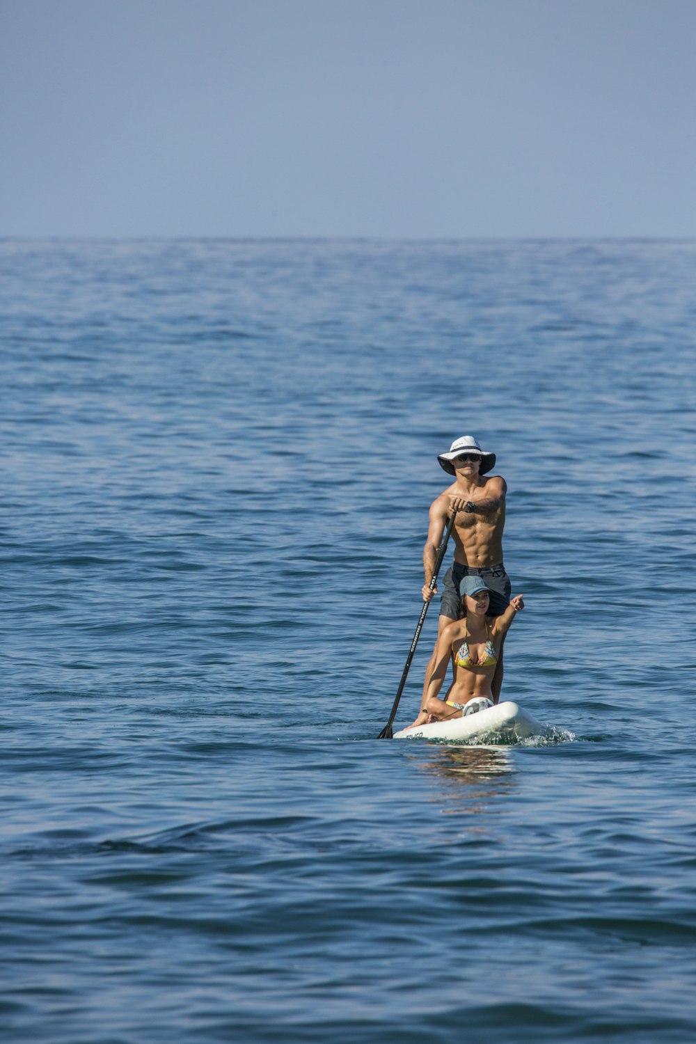 昼間の海の真ん中で白いサーフボードに青いビキニを着た女性