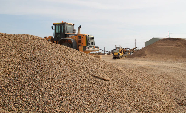 A heavy-duty truck unloading gravel at a construction site under a clear sky.