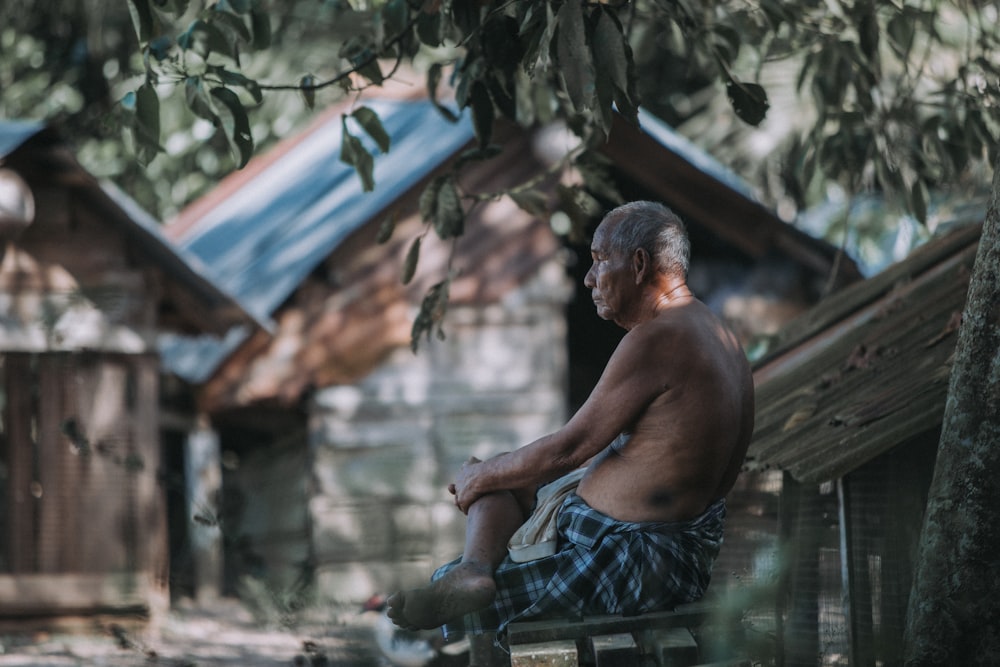 topless man in blue and white plaid shorts sitting on brown wooden bench during daytime